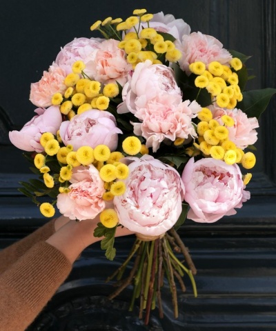 Ramo de flores cor-de-rosa e amarelas segurado por mão diante de fundo preto