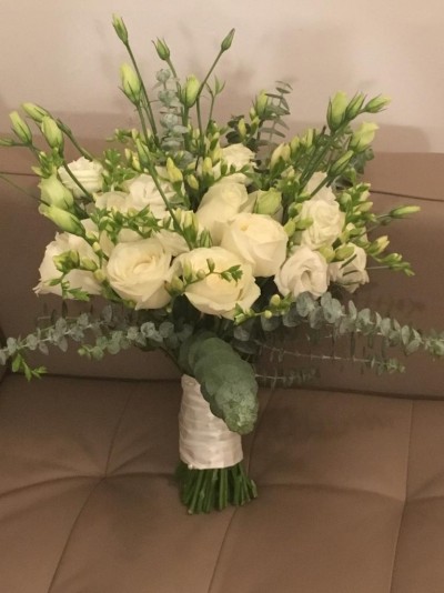 Buquê de flores brancas com folhagem verde numa fita branca sobre sofá castanho