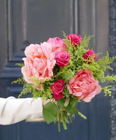 Buquê de flores rosa e verde segurado por mão em frente a porta preta