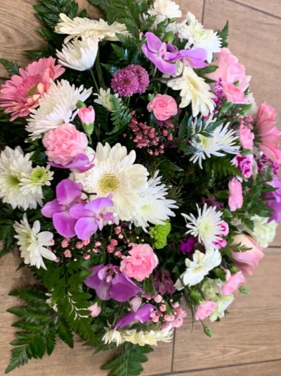 Arranjo floral multicolorido com flores brancas, rosas e lilás sobre piso de madeira.