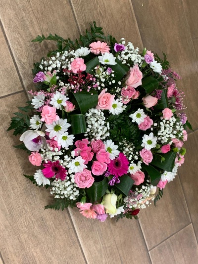 Arranjo floral redondo com rosas cor-de-rosa, margaridas brancas, flores fúcsia e folhagem verde em chão de cerâmica.