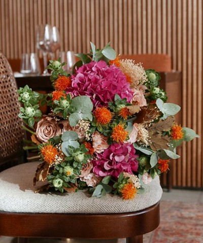 Bolsa castanha peluda com franja e alça de corrente dourada sobre cadeira.