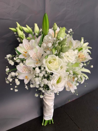 Buquê de flores brancas com rosas e lírios envolto em fita branca em fundo cinzento