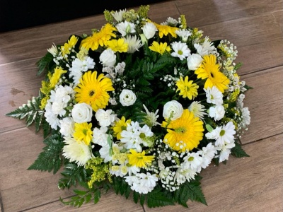 Grinalda floral com flores amarelas e brancas sobre piso de madeira.