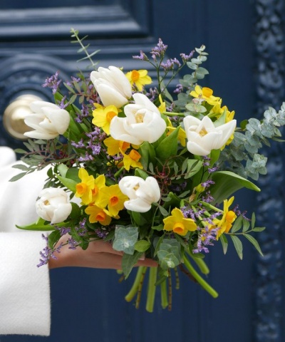 Buquê colorido de flores variadas com talos verdes na mão contra fundo azul escuro