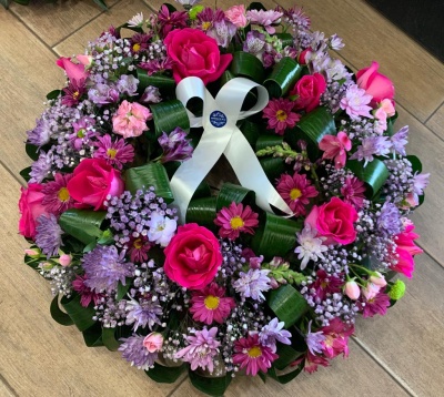 Coroa de flores colorida com laço branco sobre chão de tijoleira