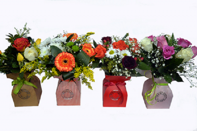 Quatro arranjos florais coloridos em caixas de papel de várias cores com laços e selo redondo.