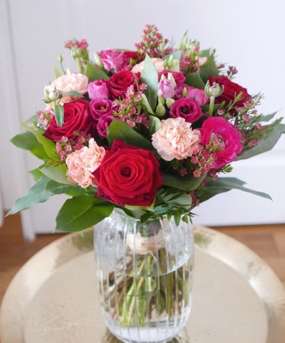 Ramo colorido de flores em vaso de vidro em mesa redonda dourada.