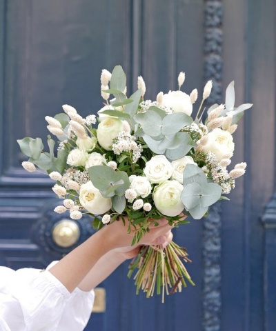Bouquet de flores brancas e verdes segurado em frente a uma porta azul