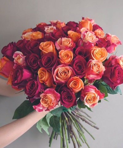 Buquê de rosas multicoloridas sendo segurado por duas mãos