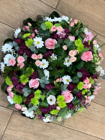 Arranjo circular de flores coloridas sobre chão de madeira