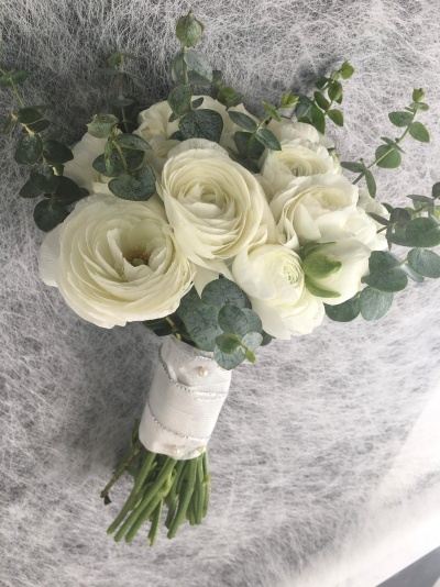 Buquê de flores brancas com folhas verdes e fita branca sobre superfície cinza