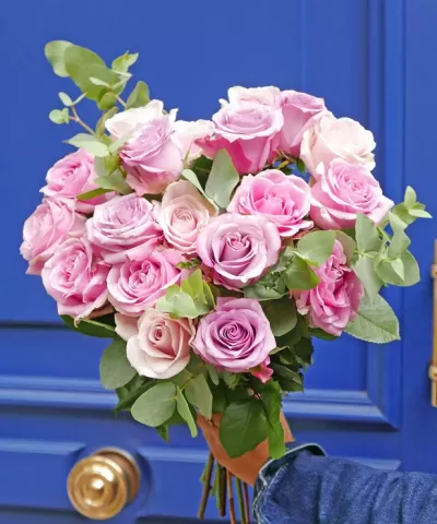 Buquê de rosas cor-de-rosa com folhas verdes numa mão diante de porta azul