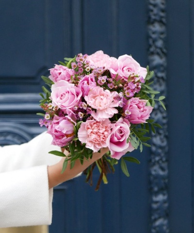 Buquê de flores rosas com folhagem verde segurado em frente a porta azul
