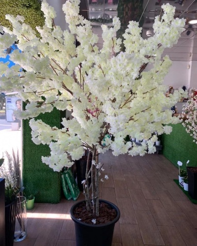 Árvore artificial com flores brancas num vaso preto em ambiente interior
