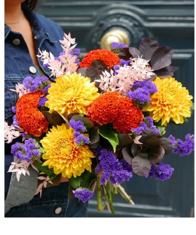 Ramo colorido de flores variadas segurado em frente a uma porta azul