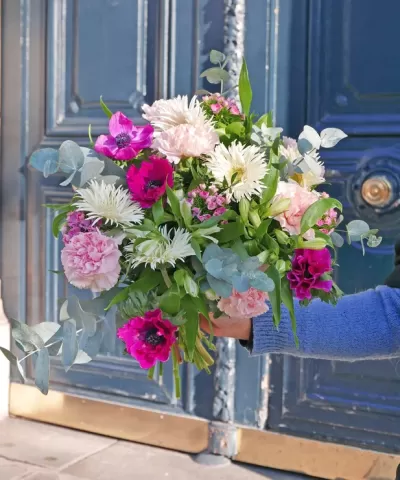Ramo de flores várias cores com folhagem segurado junto a uma porta azul