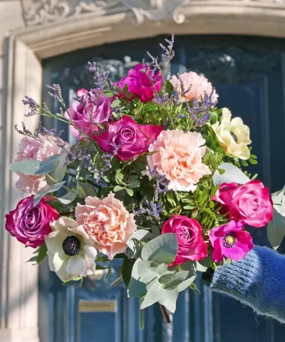 Bouquet colorido de flores diversificadas segurado junto a uma porta azul.