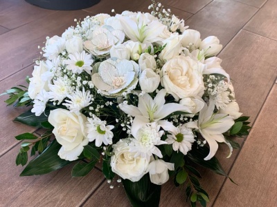 Arranjo floral com flores brancas variadas e folhas verdes sobre madeira.