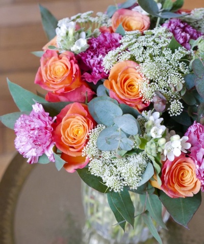 Buquê colorido em vaso de vidro com rosas e cravos, folhas verdes e flores brancas
