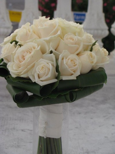 Buquê de rosas brancas com folhas verdes enroladas na base em fundo cinzento