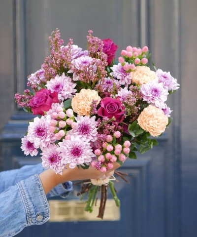 Buquê colorido de flores variadas segurado por mão com camisa de ganga