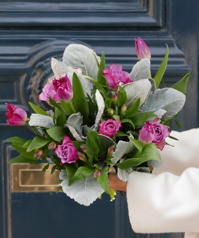 Bouquet de flores com rosas e tulipas cor-de-rosa e folhas verdes e cinzentas na frente de uma porta azul escura