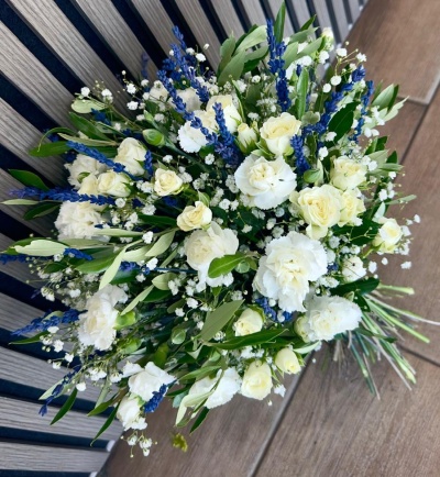 Bouquet de flores brancas e azuis com folhagem verde em banco de madeira.