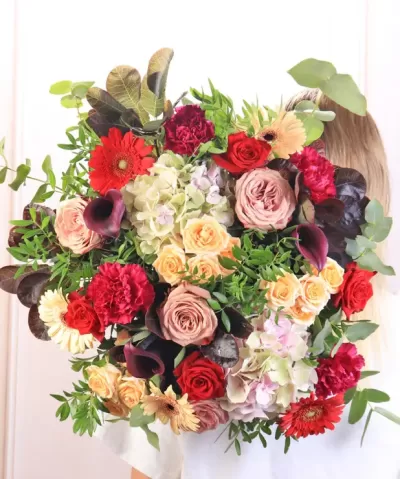 Bouquet grande colorido com várias flores e folhas verdes segurado por pessoa de camisa branca