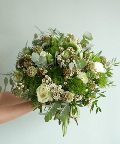 Bouquet de flores brancas e verdes com folhagens variadas num fundo cinzento claro