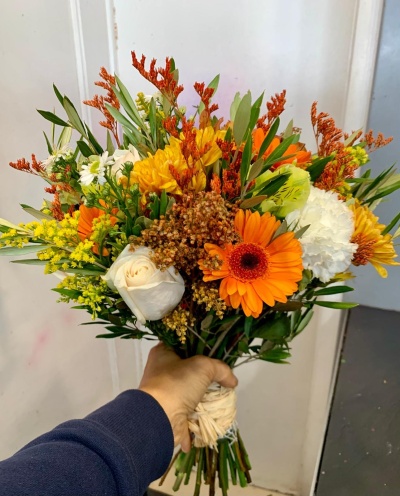 Buquê colorido de flores variadas com folhagem, segurado por uma mão