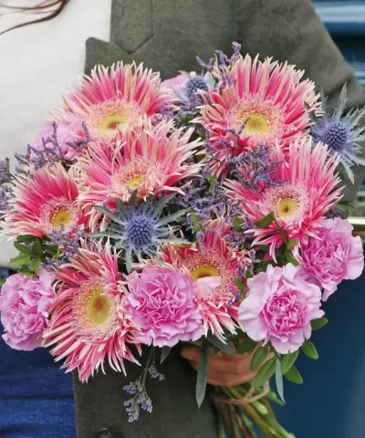 Bouquet de flores rosas com folhas verdes segurado por uma pessoa.