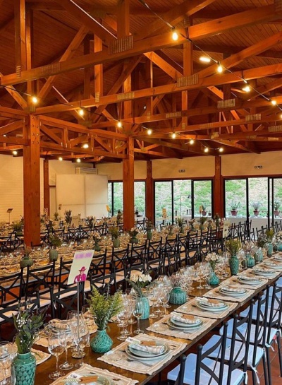 Mesa comprida posta com pratos, copos e vasos verdes decorativos em salão de madeira