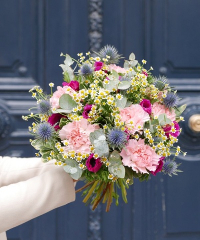 Ramo de flores coloridas com cravos e folhagem, segurado em frente a porta azul