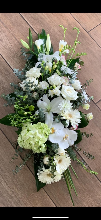 Arranjo floral com flores brancas e folhas verdes sobre chão de madeira clara