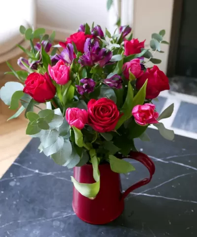 Buquê de flores coloridas em jarro vermelho sobre mesa escura