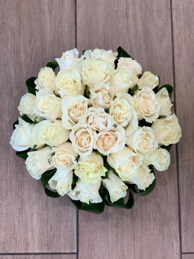 Arranjo de rosas brancas com folhas verdes em piso de madeira