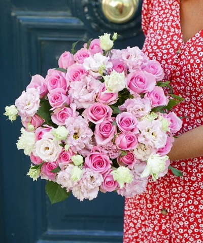 Buquê de flores rosa e branco segurado por pessoa com vestido vermelho floral em frente a porta azul