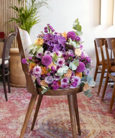 Cadeira de madeira com arranjo floral colorido sobre o assento numa sala com tapete e outras cadeiras