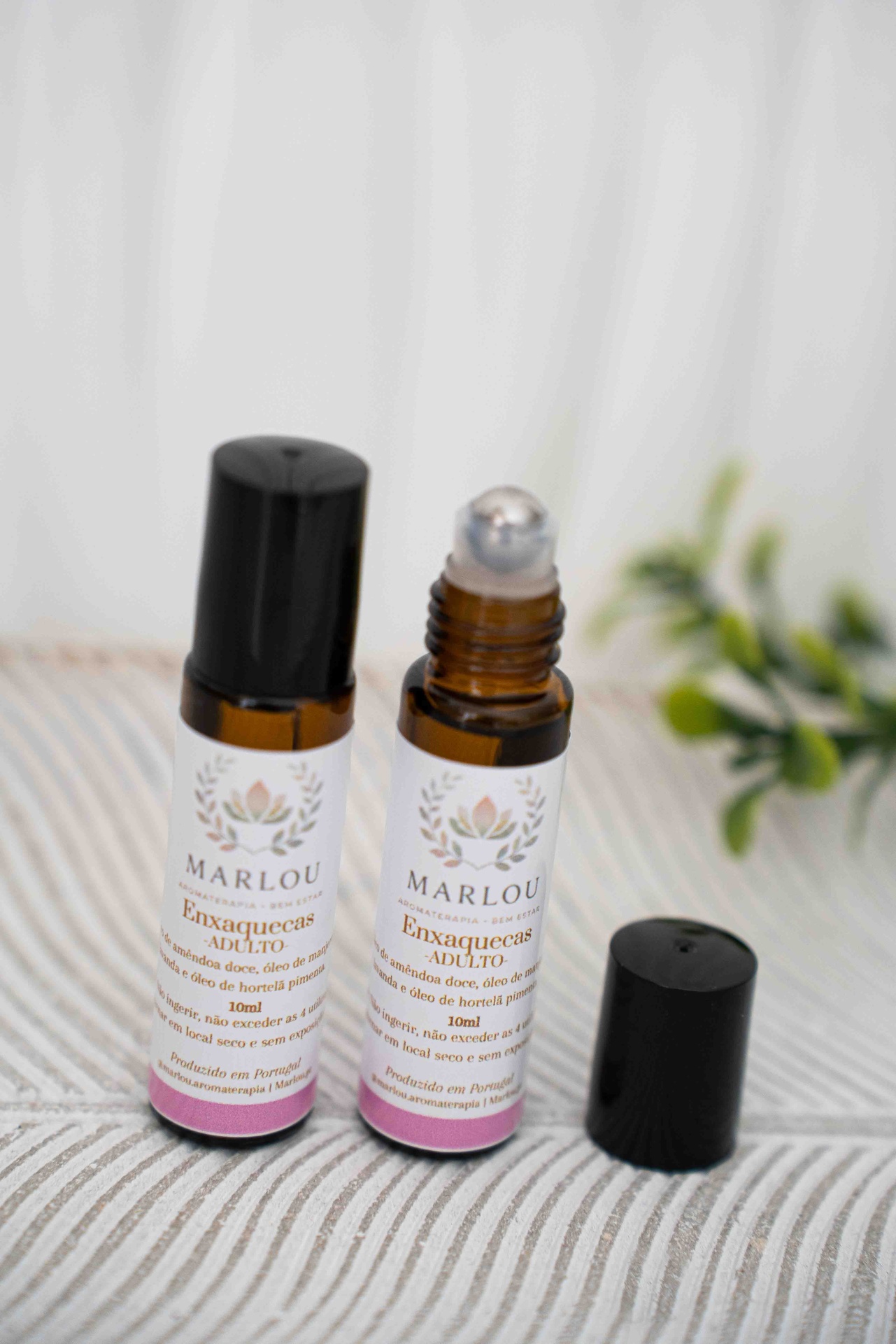 Pack enxaquecas Frascos de vidro castanho com etiquetas brancas e tampa preta, um aberto e outro fechado, sobre superfície clara com folhas verdes ao fundo.