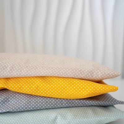 Três almofadas empilhadas com padrão de pequenos pontos brancos em fundos bege, amarelo e cinza.