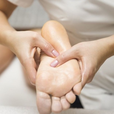 Mãos a massagear a planta de um pé descalço com fundo neutro