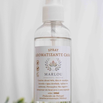 Frasco transparente de spray aromatizante com etiqueta branca e tampa branca colocado sobre madeira