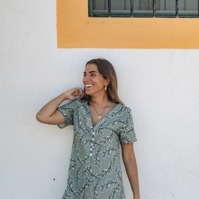 Vestido curto verde de padrão floral usado por mulher junto a parede branca e amarela