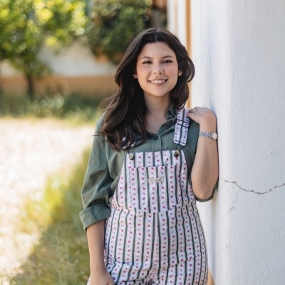 Macacão riscado branco com motivos vermelhos usados sobre camisa verde junto a parede exterior