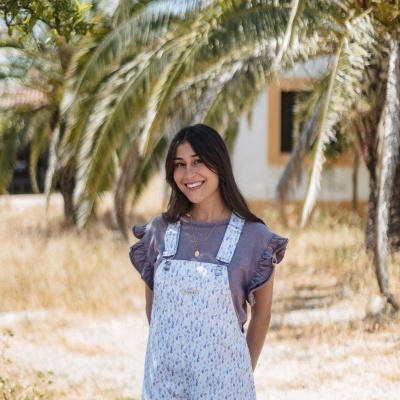 Mulher a usar macacão floral com t-shirt roxa em ambiente exterior com palmeiras