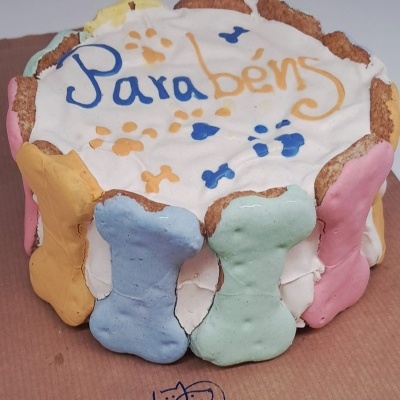 Bolo branco com ossos coloridos decorativos e texto Parabéns no topo.