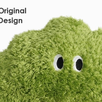 Peluche verde felpudo com olhos bordados ao lado do texto Original Design