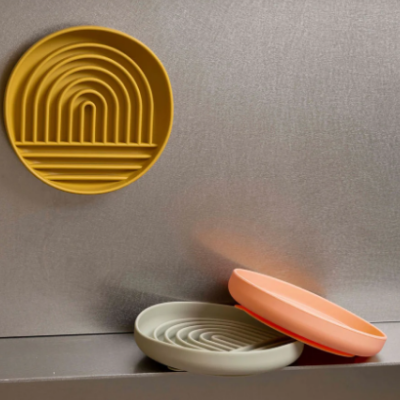 Três pratos redondos de silicone com relevo tipo arco-íris em amarelo, cinza e laranja