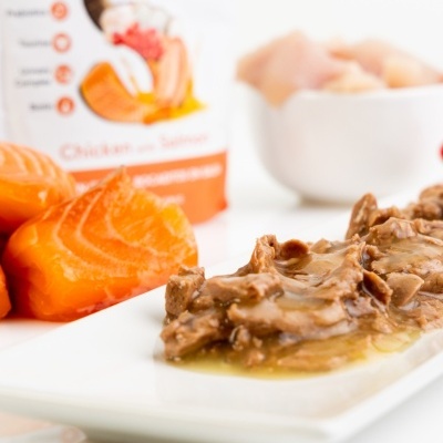 Refeição húmida para animais com carne em molho, pedaços de salmão e embalagem com texto Chicken with Salmon e marca Dibaq.